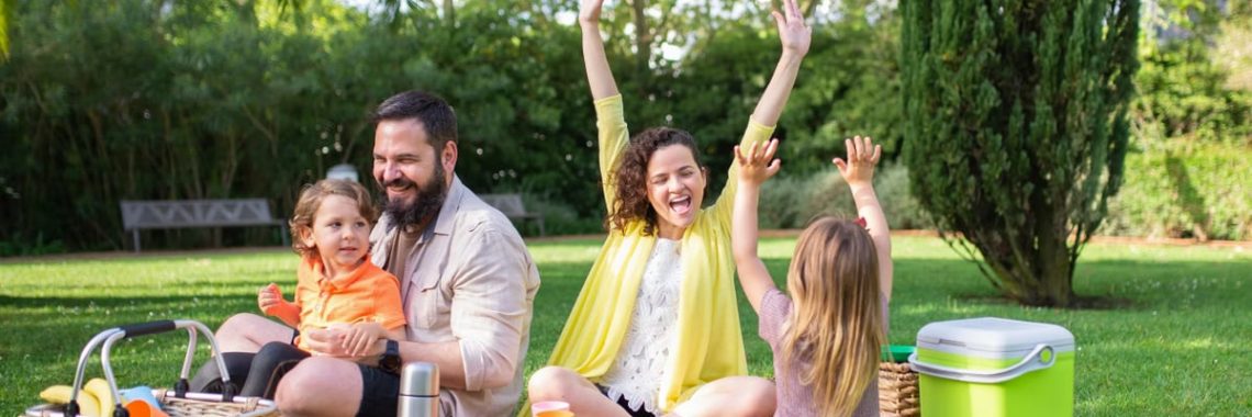 Happy family enjoying a sunny picnic with children on a blanket in a Portugal park.